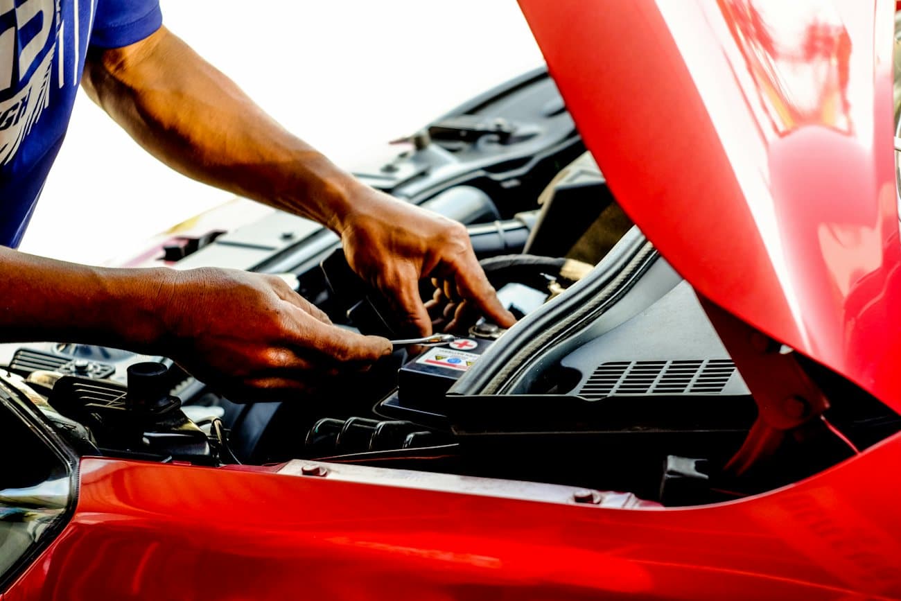 Hands working on a car battery under an open hood