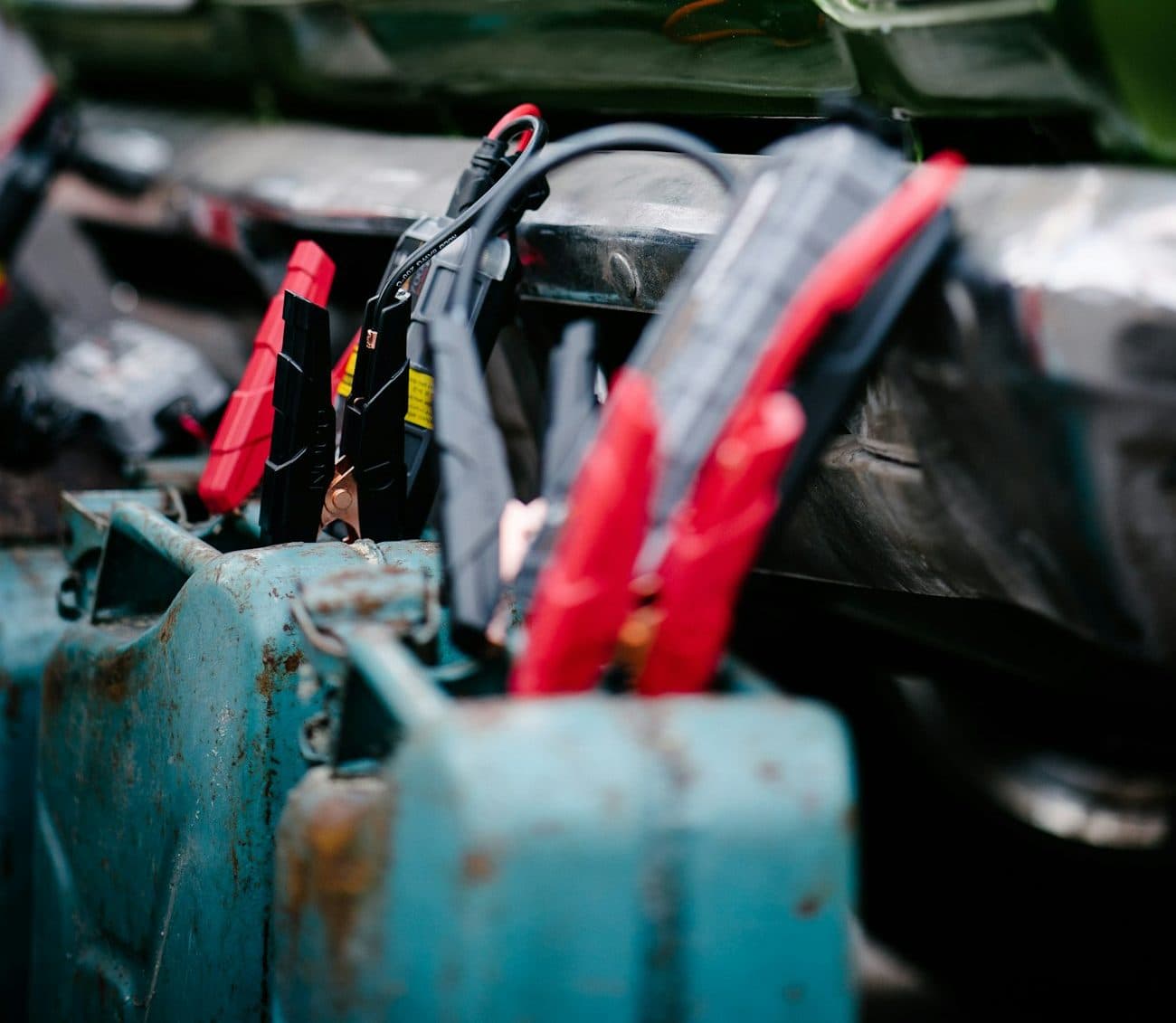 Red jumper clamps and a portable jump starter beside a vehicle